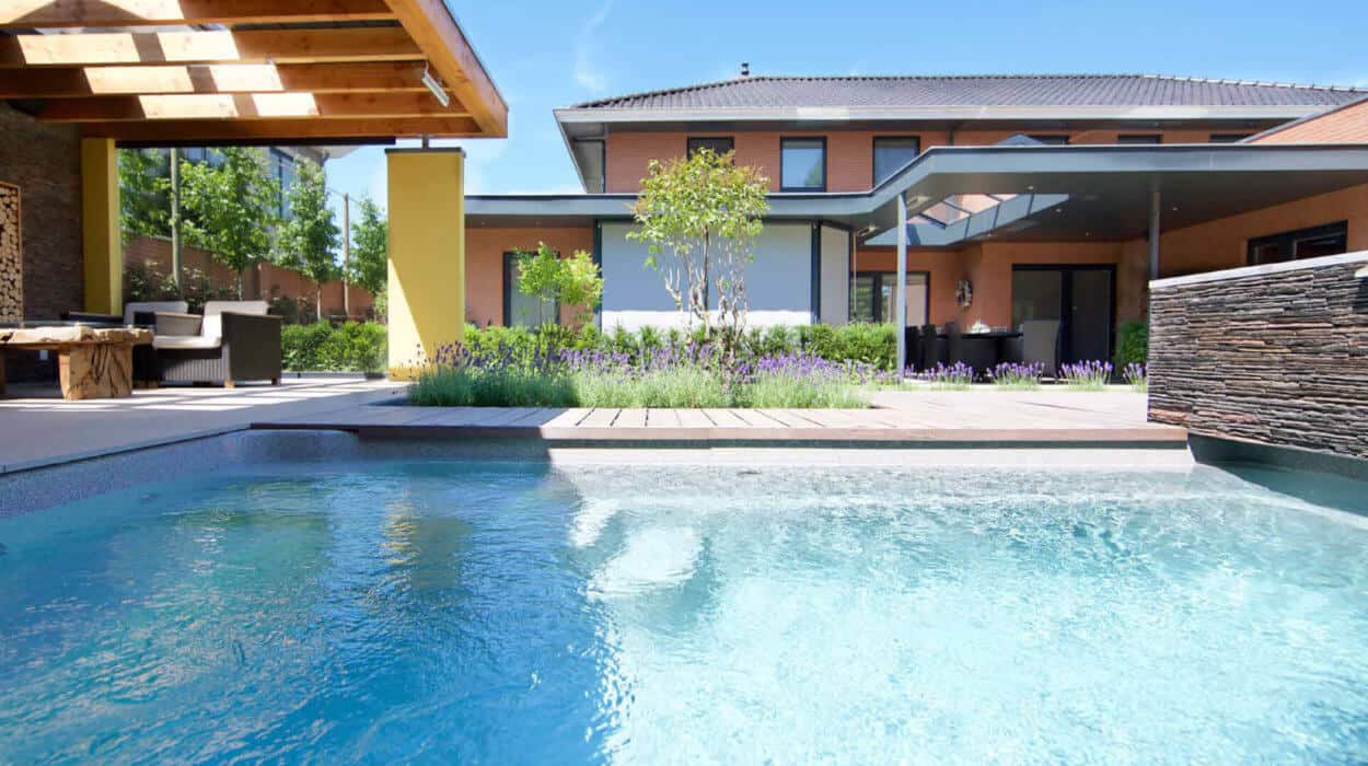 Modern family home with a contemporary garden and a clear turquoise swimming pool surrounded by decking and lush greenery.