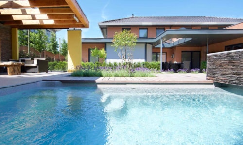 Modern family home with a contemporary garden and a clear turquoise swimming pool surrounded by decking and lush greenery.