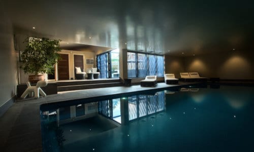 Contemporary basement indoor swimming pool with modern lounge seating and mood lighting.
