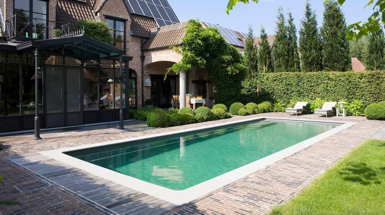Traditional-style brick house with solar panels and a rectangular garden pool bordered by lush greenery and brick paving.