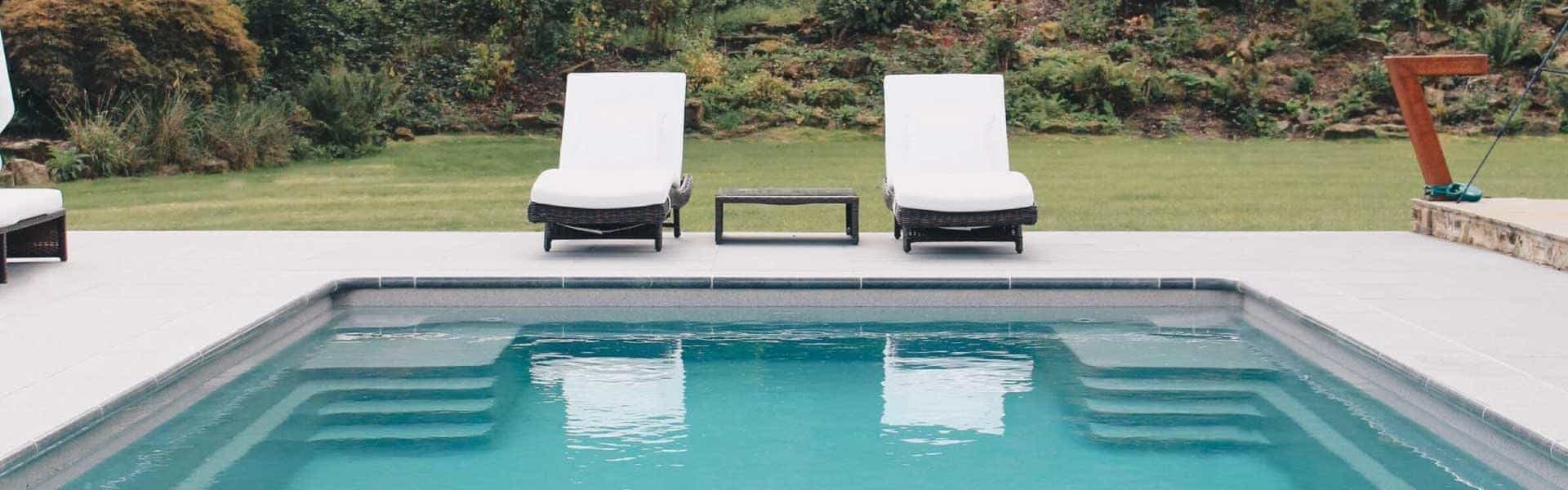 Elegant garden pool with two white sun loungers overlooking manicured lawns and leafy trees.