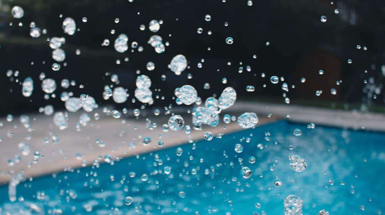 Close-up of water droplets splashing beside a bright blue outdoor swimming pool.