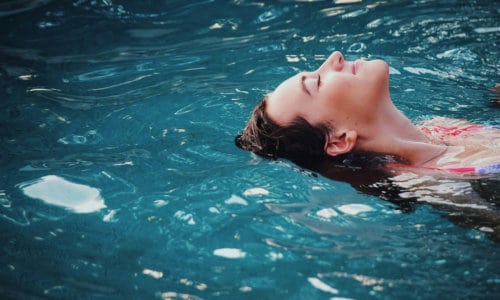 Woman floating peacefully on her back in clear blue pool water.