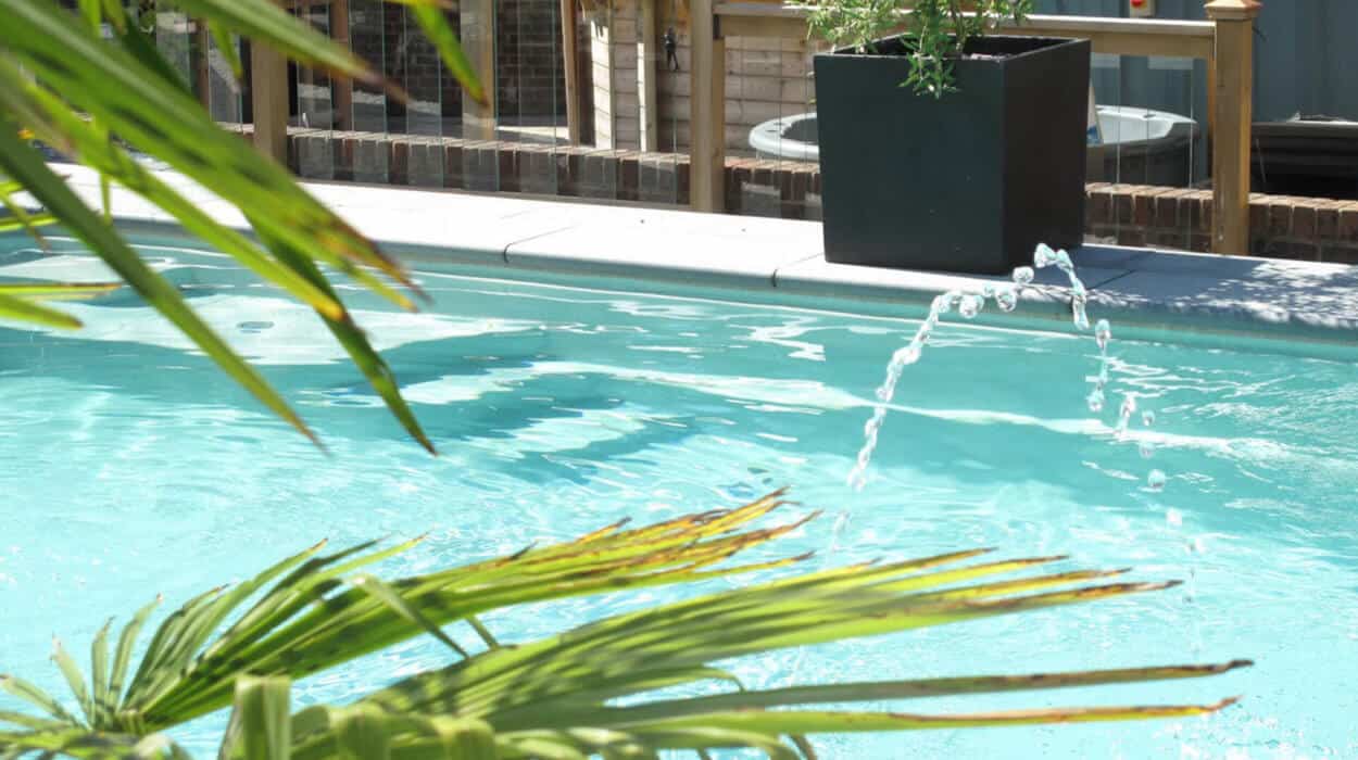 Modern garden pool with a gentle water feature surrounded by tropical plants and natural wood decking.