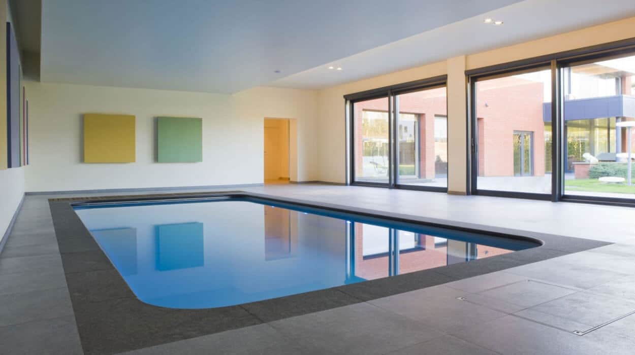 Modern indoor swimming pool with clean architectural lines, large windows, and minimalist wall art.
