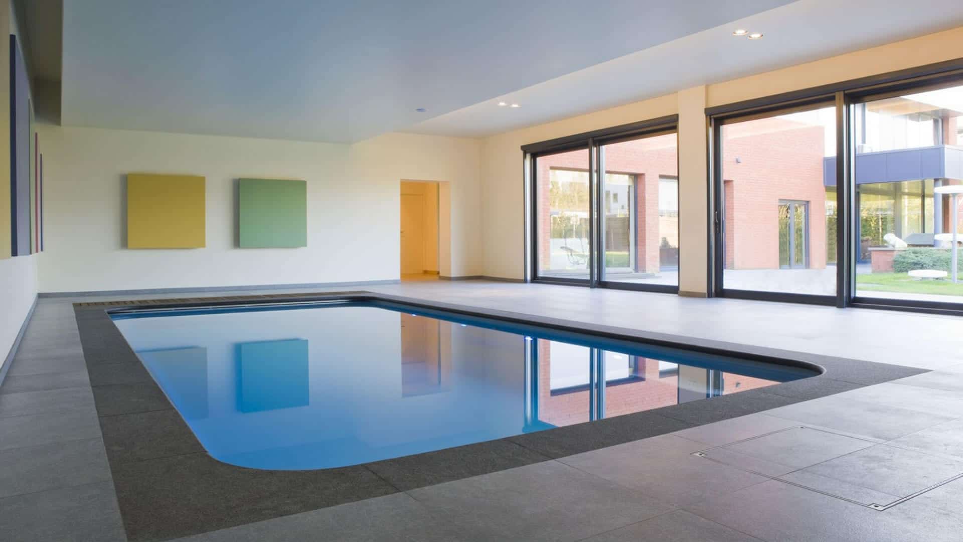 Modern indoor swimming pool with clean architectural lines, large windows, and minimalist wall art.